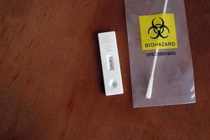 Coronavirus - COVID-19 - rapid test with positive result next to a nasal swab in a transparent bag with bio hazard photo