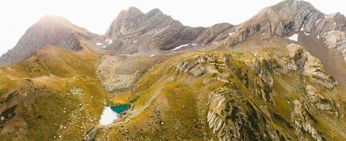 Mountains green lake with reflections and rocky shore in autumn time. Wild nature and rural mount valley. Fall grey weather rainy clouds on sky. Cold lake, winter coming landscape photo