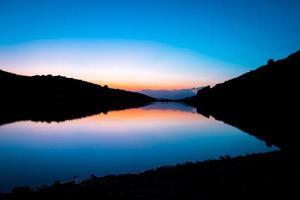 Blue mountain lake in blue hour wit orange after sunset light autumn time. Wild nature and rural mount valley photo