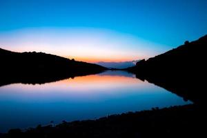 lago de montaña azul en hora azul ingenio naranja después de la luz del atardecer tiempo de otoño. naturaleza salvaje y valle de monte rural foto