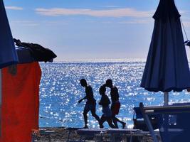 group of boys strolling on the sand of a beach of the Italian Ligurian Riviera in the height of summer 2022 photo