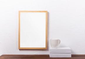 White frame mockup hanging on the wall with stack of books and coffee cup photo