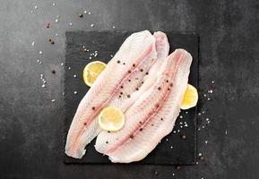 Raw pangasius fish fillet with lemon and spice on state plate on concrete background