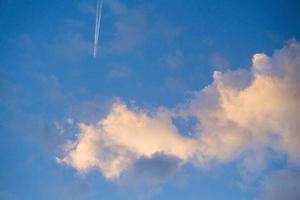 Trace of the airplane in the morning blue sky, white contrail trail of the plane flying in the clouds, beautiful fluffy skies, cloudscape background. photo