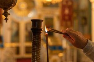 Iglesia Ortodoxa. cristiandad. mano del sacerdote encendiendo velas encendidas en la iglesia ortodoxa tradicional en la víspera de pascua o navidad. religión fe orar símbolo. foto