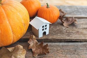 Autumnal Background. Toy house and pumpkin on wooden background. Thanksgiving banner copy space. Hygge mood, change of seasons concept. Hello Autumn with family Halloween party. photo