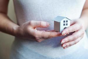 Female woman hands holding small miniature white toy house. Mortgage property insurance dream moving home and real estate concept. photo