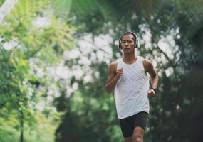 el deportista asiático se ajusta al cuerpo con auriculares blancos y un reloj inteligente mientras corre o trota en el jardín, tiene más árboles y aire limpio, hace ejercicio en el parque. concepto de carrera deportiva saludable. foto