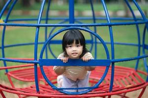 linda chica asiática sonríe y juega en la escuela o en el jardín de infantes o en el patio de recreo. Actividad de verano saludable para niños. niña asiática escalando al aire libre en el patio de recreo. foto