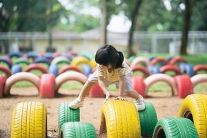 Cute asian girl smile and play on school or kindergarten yard or playground. Healthy summer activity for children. Little asian girl climbing outdoors at playground. photo