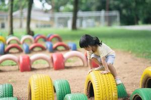 Cute asian girl smile and play on school or kindergarten yard or playground. Healthy summer activity for children. Little asian girl climbing outdoors at playground. photo