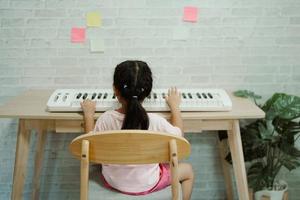 Asian cute girl learning online piano music with teacher by mobile phone or tablet. The idea of activities for the child at home during quarantine. Music learning study online concept. photo