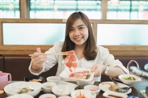 Asian woman eating a sashimi salmon. Woman using chopstick to pick raw fish sashimi from white bowl. Woman using chopsticks sliced raw salmon, Japanese food in a japanese restaurant. photo