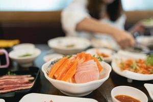 Asian woman eating a sashimi salmon. Woman using chopstick to pick raw fish sashimi from white bowl. Woman using chopsticks sliced raw salmon, Japanese food in a japanese restaurant. photo