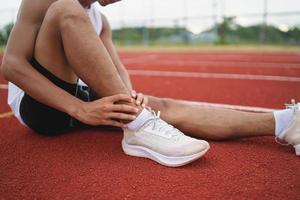 atletas deportistas corredores con ropa deportiva blanca sentado esguince de tobillo sintiendo dolor en el tobillo o la pierna o la rodilla después de practicar en la pista de atletismo en el estadio, copiar espacio. concepto de lesión deportiva del corredor. foto