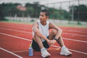 atletas corredor deporte hombre descansando botella agua cansado y sediento practicando en una pista de atletismo en un estadio. correr entrenamiento beber agua. concepto de carrera de hombre deportivo. foto