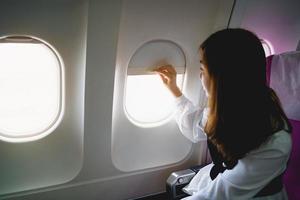 Asian woman sitting in a seat in airplane and looking out the window going on a trip, asian woman passenger is leaving for a trip by plane on vacation. Vacation travel concept. photo