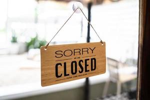 Close sign broad through the door glass. CLOSED sign board through the glass of store window. closed we are sorry text wooden board  door vintage shop sign close store. photo