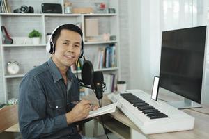 Asian man wearing white headphones compose song and learning online or record sound with a microphone and use computer recording music program. sound engineer man record music. photo
