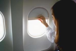 Asian woman sitting in a seat in airplane and looking out the window going on a trip, asian woman passenger is leaving for a trip by plane on vacation. Vacation travel concept. photo