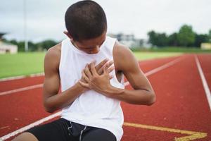 atletas asiáticos deportistas corredores sentados con dolor en el pecho debido a una enfermedad cardíaca o un ataque cardíaco después de practicar en la pista de atletismo en el estadio, copie el espacio. concepto de lesión deportiva del corredor. foto