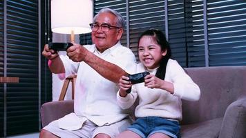 el abuelo y la nieta se divierten jugando videojuegos juntos en la sala de estar de casa. foto