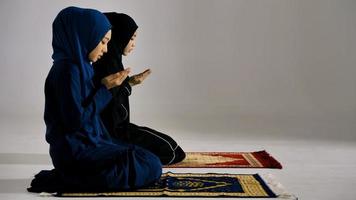 Two Asian Muslim young women in traditional hijab are praying glorify Allah and practicing the Islamic faith in mosque. photo