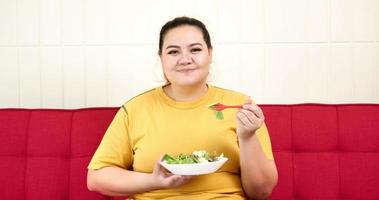 mujer gordita sentada en un sofá y comiendo ensalada. foto