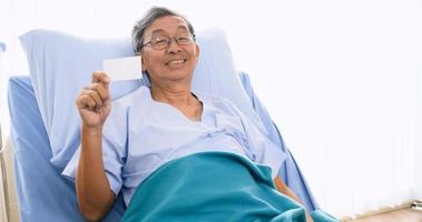 Male patient smiling and holding card on sickbed in hospital room. photo