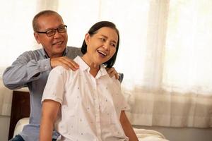 feliz marido asiático masajeando el hombro de su esposa en la casa. foto