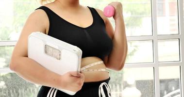 Chubby woman doing exercise by dumbbell and holding a scale. photo