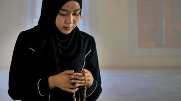 Asian Muslim young woman in black traditional hijab praying with Islamic beads in mosque. photo