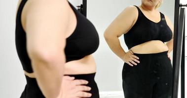 Chubby woman standing and looking at her stomach in a mirror. photo