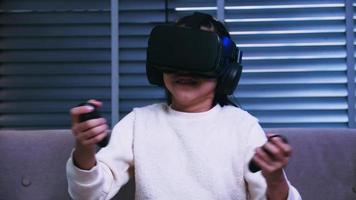 niña asiática divirtiéndose jugando videojuegos con gafas de realidad virtual en el sofá en casa. foto