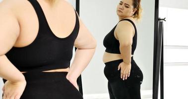 Chubby woman standing and looking at her stomach in a mirror. photo