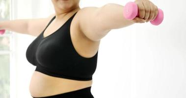 Chubby woman doing exercise by dumbbell in a room. photo