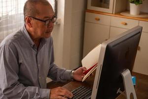Asian businessman typing on a computer keyboard and holding a book in the office room. photo
