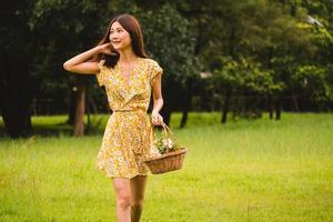 Beautiful woman in yellow dress holding a basket with flowers standing on grass in the park photo