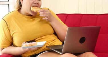 Chubby woman eating donuts and surfing internet on a sofa in a room. photo