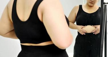 Chubby woman standing and looking at her stomach in a mirror. photo