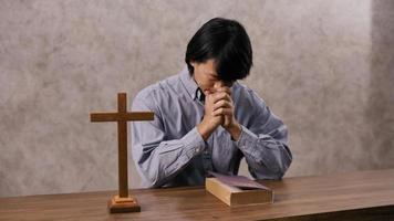 A young Asian Christian man praying to Jesus Christ in a church.