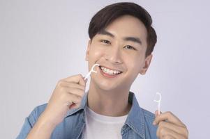 Young smiling man holding dental floss over white background studio, dental healthcare and Orthodontic concept. photo