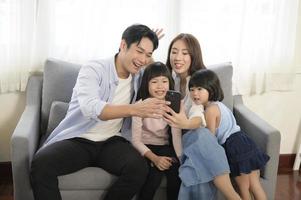 Asian family with children holding smartphone and making video call at home photo