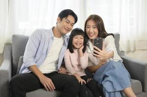 Asian family with children holding smartphone and making video call at home photo