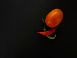 tomates naturales y chiles sobre un fondo oscuro. vista superior con fondo de comida, mesa de piedra negra, espacio de copia. foto