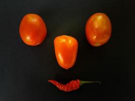 Natural tomatoes and chilies on a dark background. Top view with food background, black stone table, copy space. photo