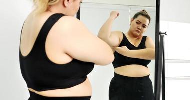 mujer gordita de pie y mirando su brazo en un espejo. foto