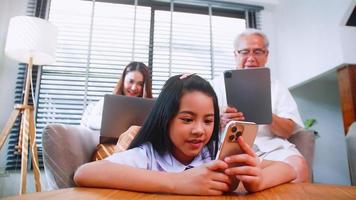 el abuelo, la madre y la hija usan tecnología inalámbrica mientras se relajan en la sala de estar. la familia asiática disfruta de la tecnología móvil moderna en su hogar. foto