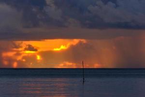 Rain from orange sky over ocean at sunset photo