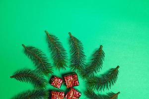 Top view of Christmas gift box red balls with spruce branches and bell on green background. photo